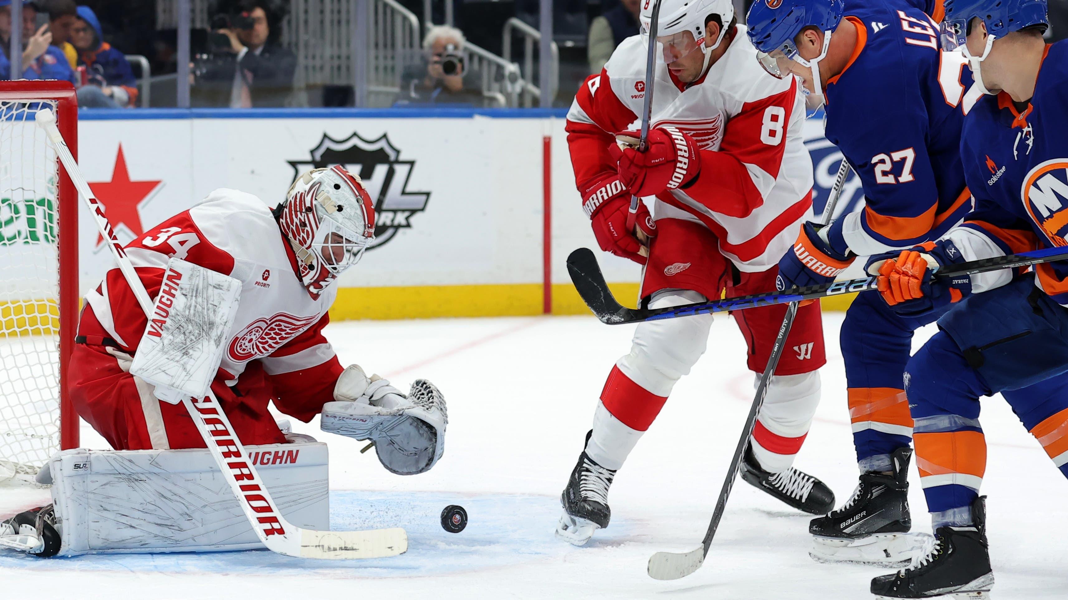 Detroit Red Wings goaltender Alex Lyon (34) plays the puck against New York Islanders left wing Anders Lee (27) and center Jean-Gabriel Pageau (44) during the second period at UBS Arena / Brad Penner - Imagn Images