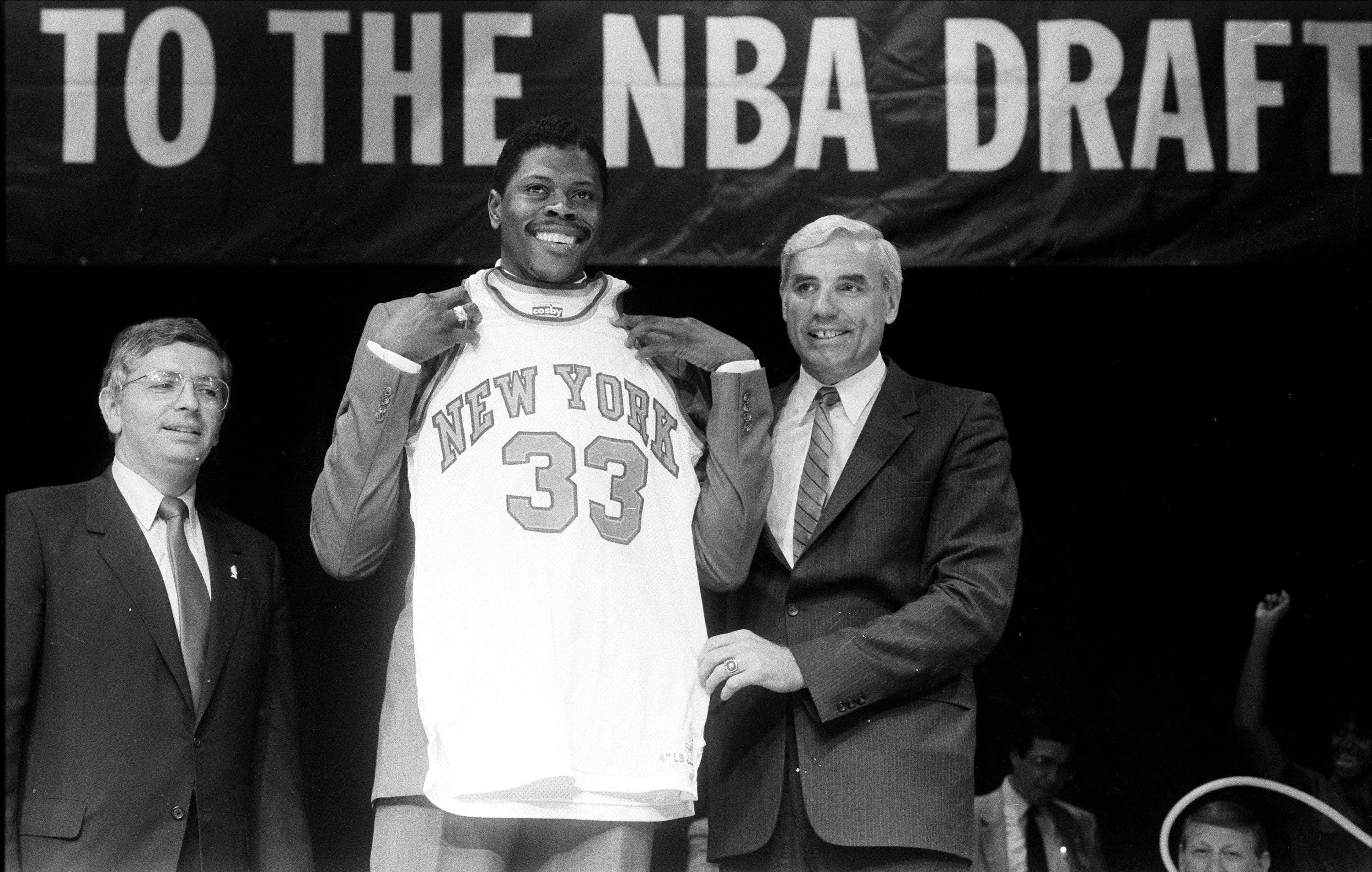 Patrick Ewing towers over Knicks VP Dave DeBusschere as he tries on New York Knicks jersey for size, with David Stern alongside. / Willie Anderson/NY Daily News Archive via Getty Images