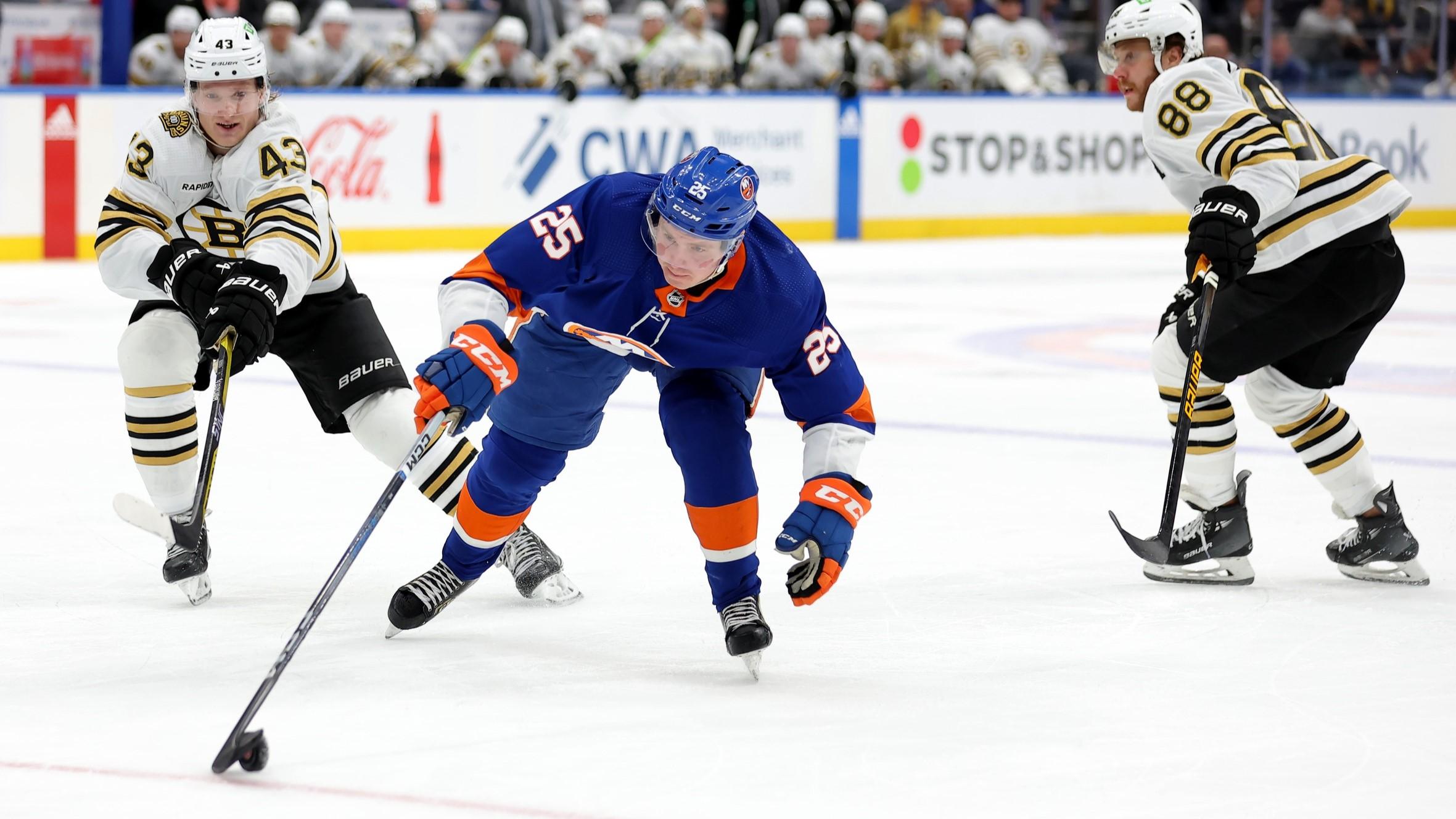 Dec 15, 2023; Elmont, New York, USA; New York Islanders defenseman Sebastian Aho (25) plays the puck against Boston Bruins left wing Danton Heinen (43) and right wing David Pastrnak (88) during the second period at UBS Arena. / Brad Penner-USA TODAY Sports